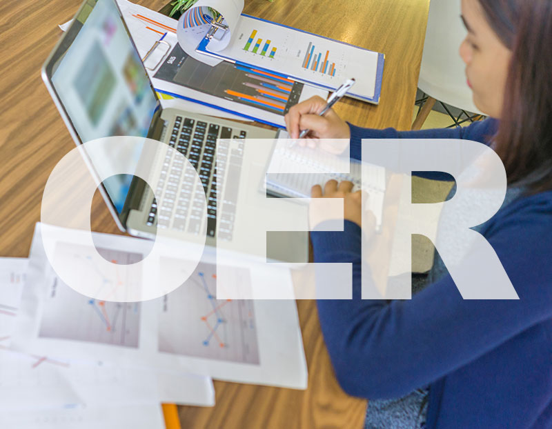 Person at computer desk with computer and papers with words "OER" in front of her