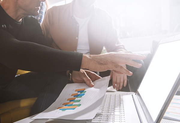 Person points at computer screen with papers that feature charts