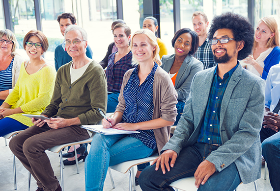 Numerous people sit at desks look up front and smiling