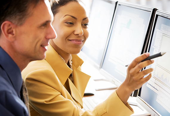 Person points to computer screen with pen while another person looks at computer smiling