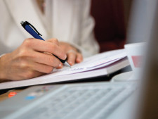 Person writes in notebook while multiple choice exam sits on desk