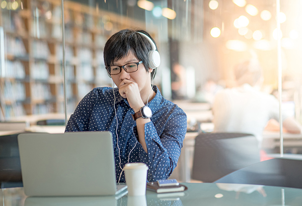 Student sits in library looking at computer screen quizzically