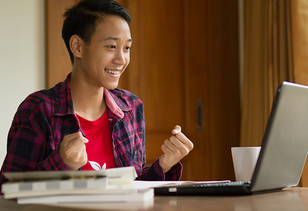 Student looks at computer with fists of success while smiling