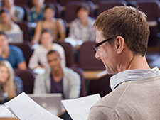 Group of students are blurred in background while teacher looks at papers