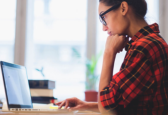 Person sits at desk with hand on chin looking at computer