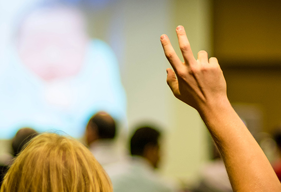 Person raises hand during class with projector screen in background