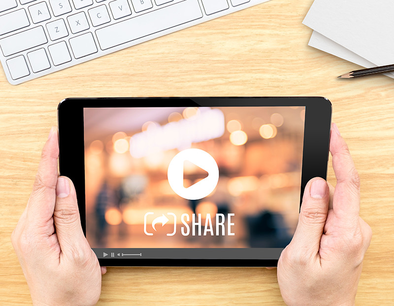 Person holds tablet with a play screen on the table and the word "share"