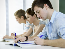 Group of students sit in line and look down at booklet with pens in hand