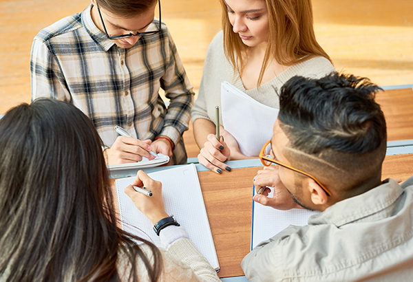 Four students sit at table with drawing pads and pencils