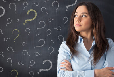 Instructor stands with back to chalkboard with question marks written all over the board