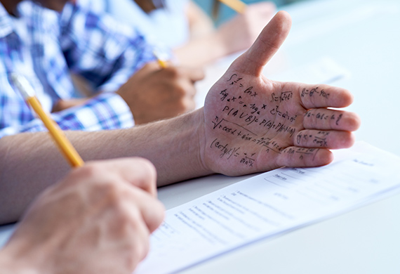 Student takes test and looks at hand with cheat notes written on hand