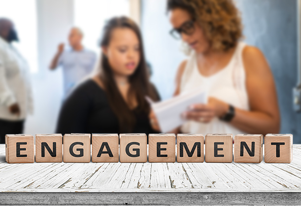 People in background are blurred with letter blocks in the forefront spelling, "engagement"