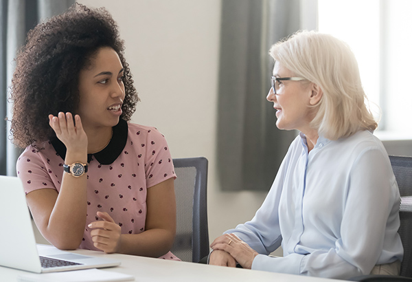 Younger student sits down with older woman to talk with computer on table