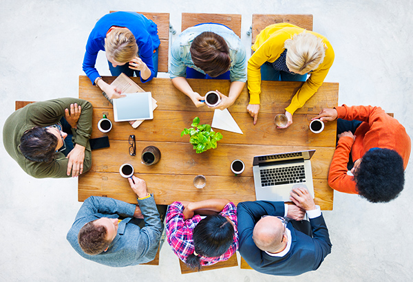 Employees collaborate around table with coffee discussing work