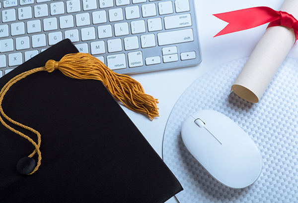 Graduation cap, computer keyboard, diploma and computer mouse lay on table