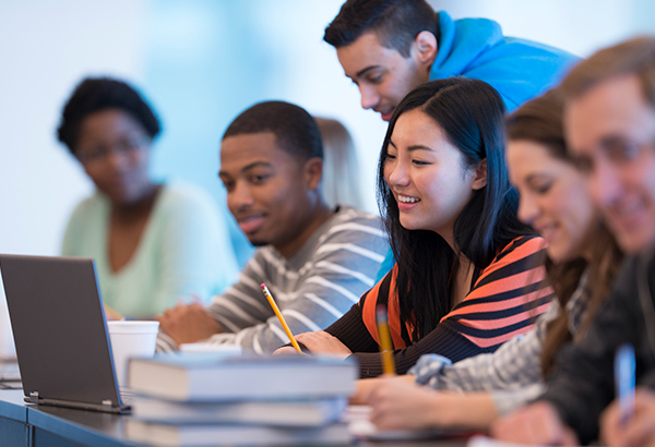 Students sit around table sharing computer while taking notes