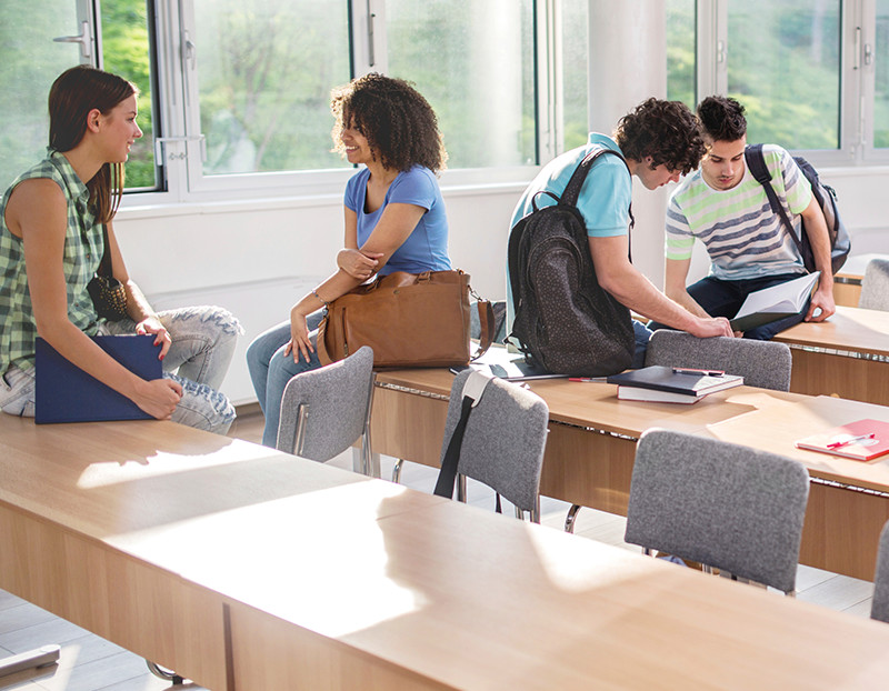 Students talk amongst each other sitting casually on desks and chairs before class starts