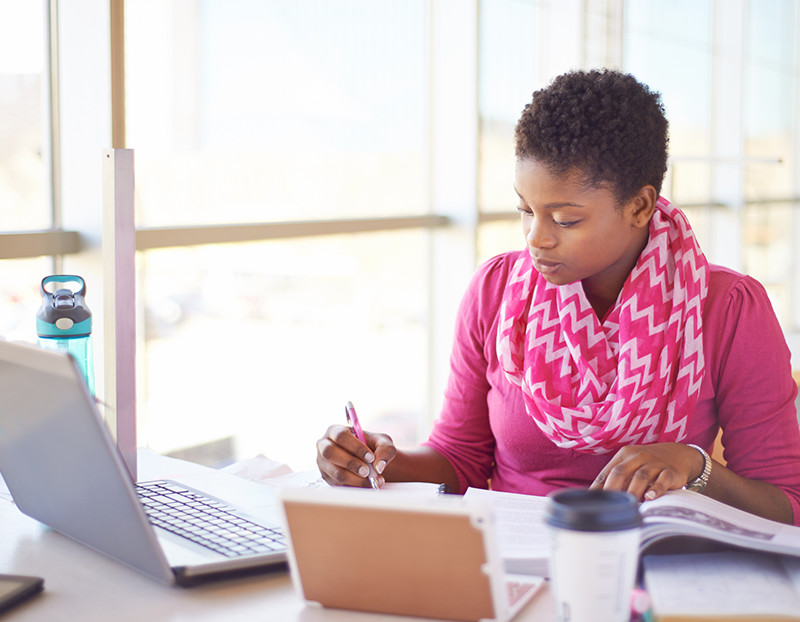 Instructor writes at desk with laptop opened