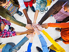 Students from all ethnicities put their hands together in circle