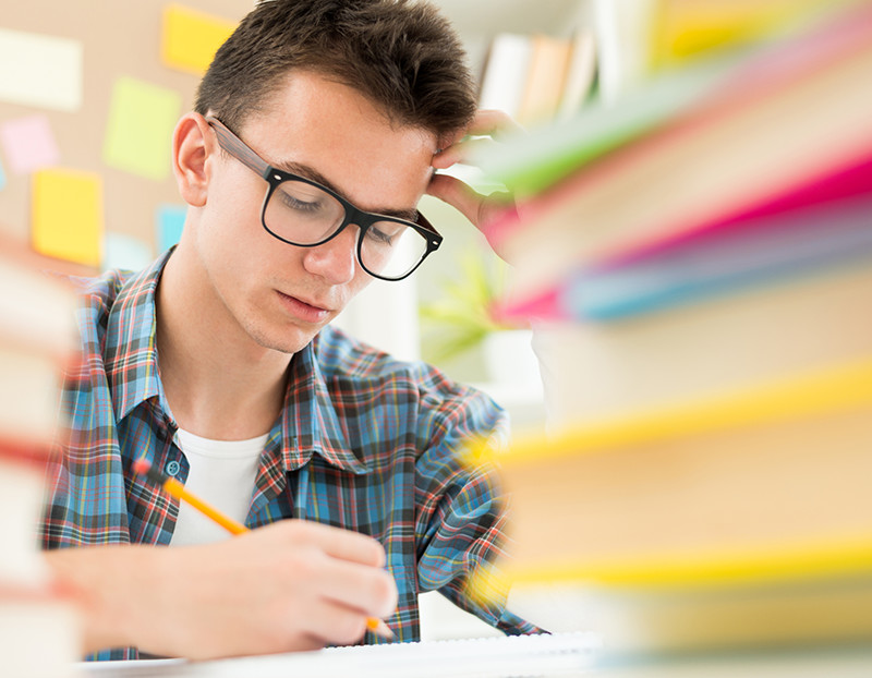 Student concentrates on assignment with books, stickies and papers blurred around them