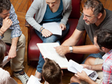 People sit in a circle on chairs holding paper and notes in their hands and laps