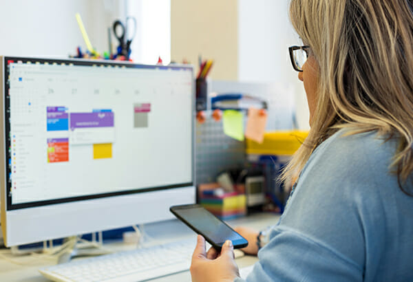 Person looks at phone in hand and calendar events on computer