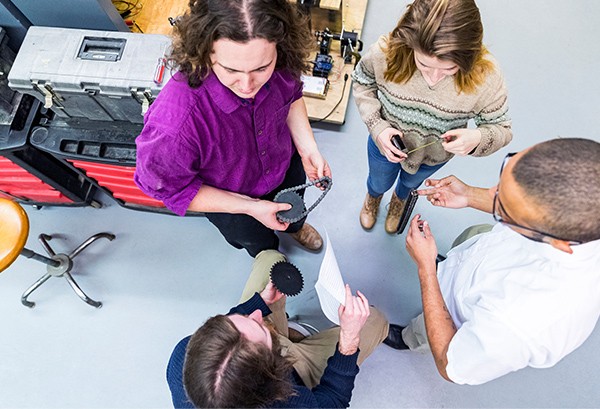 engineering-students-discussing-problems-holding-gears-machine-parts