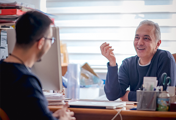 older man-at-desk-smiling-talking-with-younger-man-with-glassess-at-desk